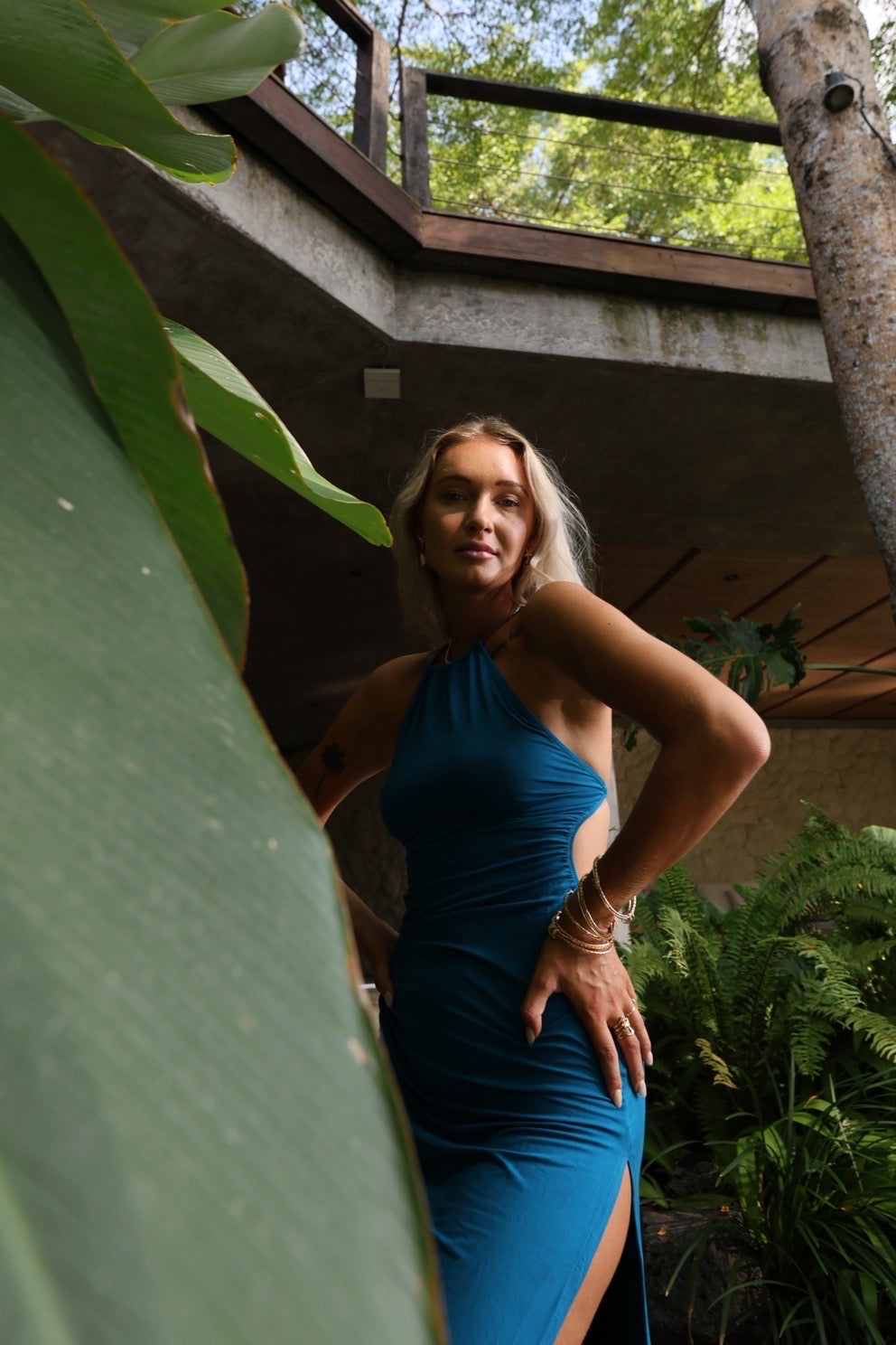 Woman in a blue dress standing among greenery with a building in the background